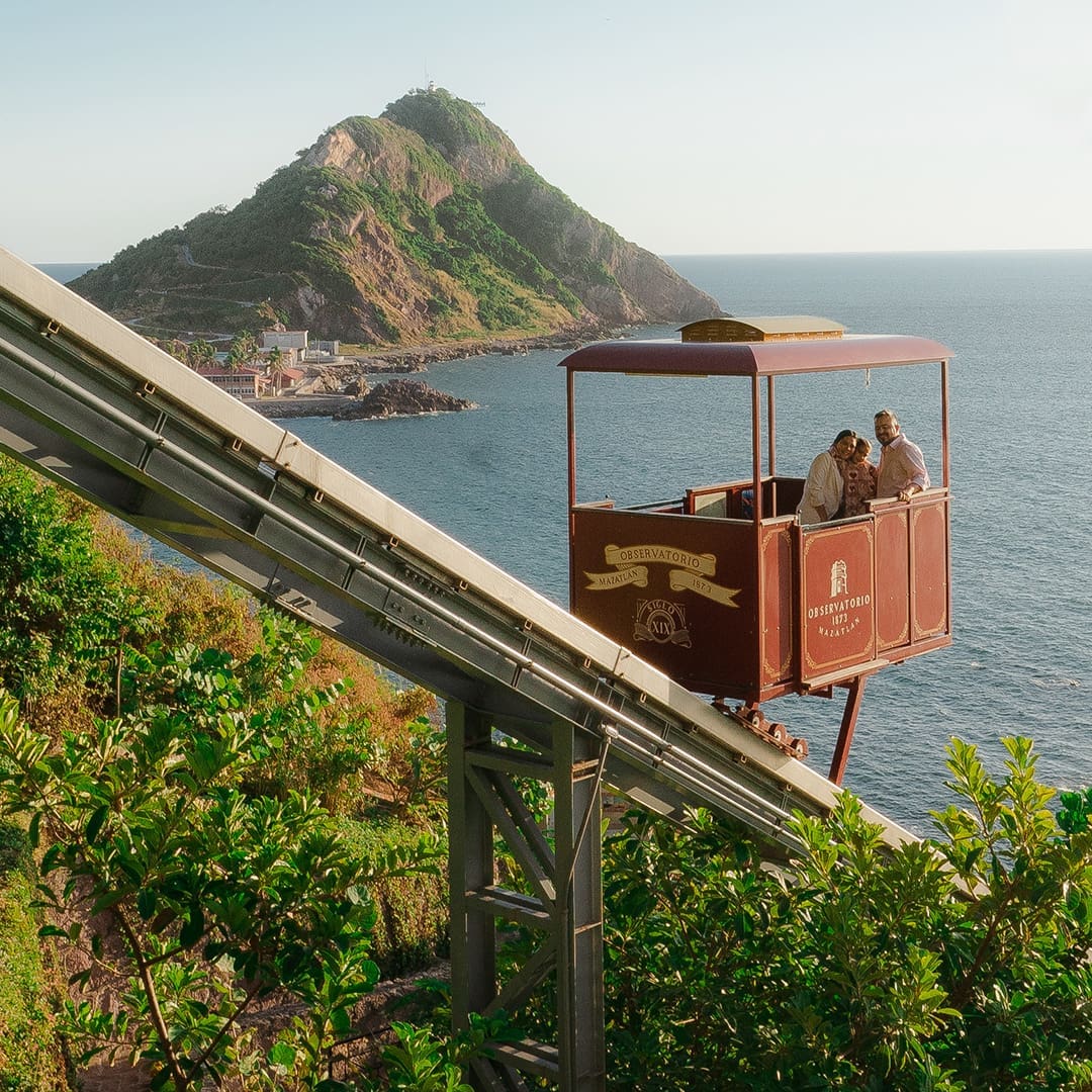 Family rides in commercial inclined funicular tram car with tropical mountain and ocean views in the background from Mazatlan, Mexico
