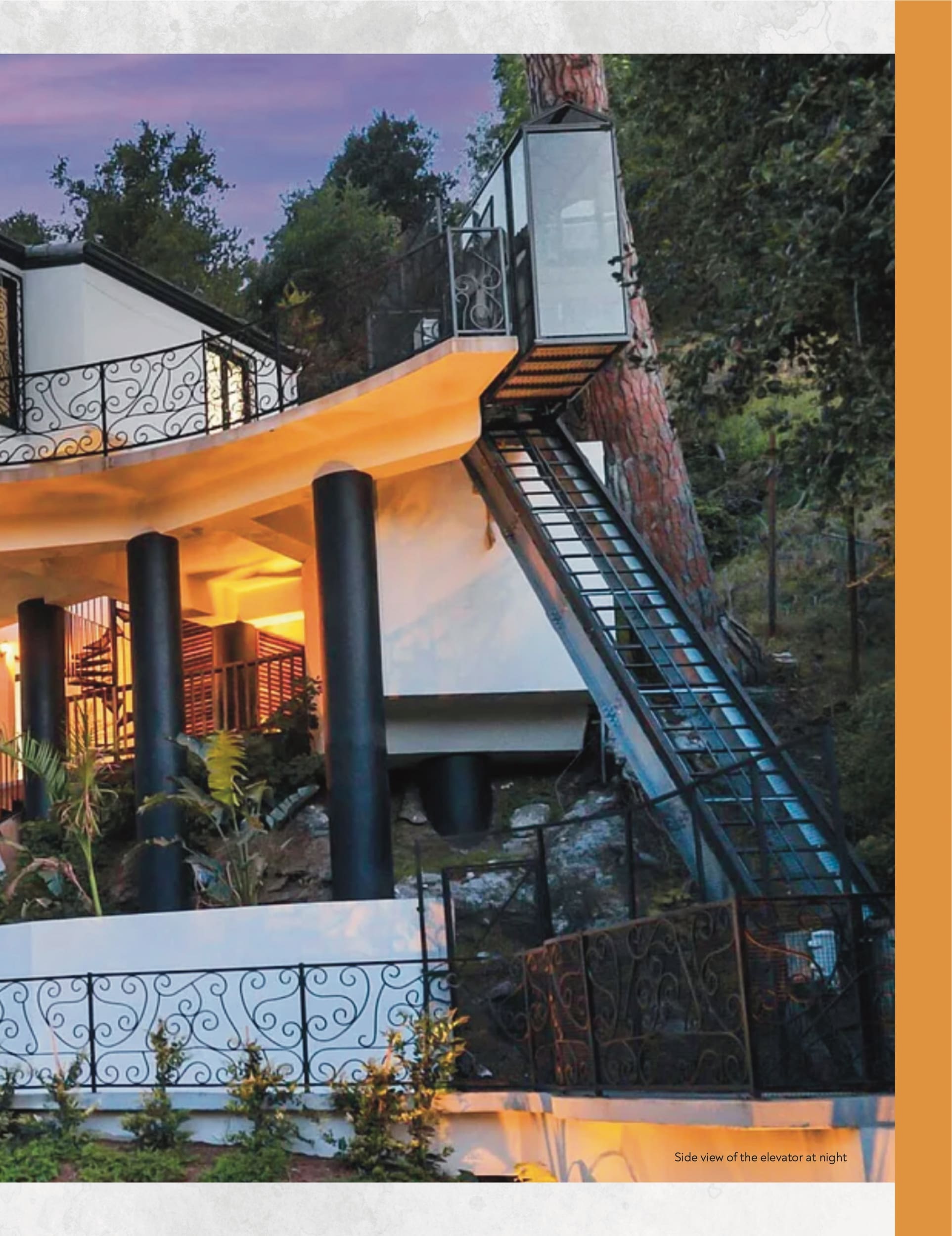 Page 2 of the July 2026 Elevator World magazine feature on Hill Hiker's Beverly Hills residential inclined elevator, Full-page photograph showing a nighttime side view of the Hill Hiker installed alongside the Beverly Hills home.