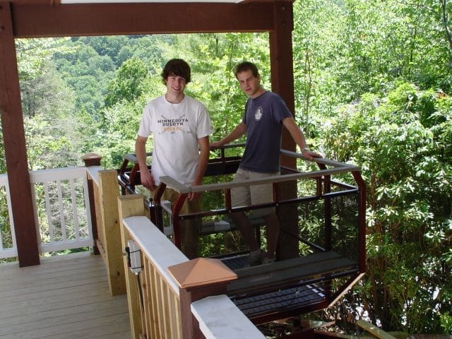 Hillside funicular lift parked at top of a covered upper landing area with wood railing and two riders on board the car